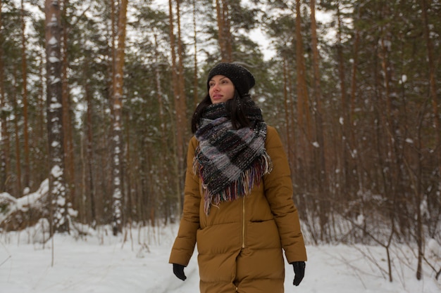 Una giovane ragazza con un cappello nero e una giacca marrone cammina attraverso la foresta di neve invernale. Foresta invernale. Paesaggio invernale.