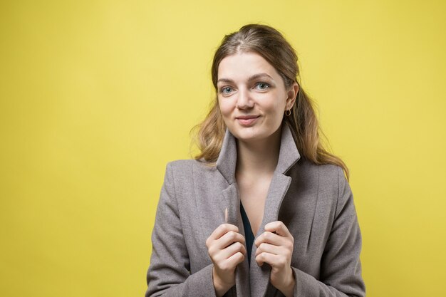 Una giovane ragazza con un cappotto posa in uno studio su uno sfondo giallo.