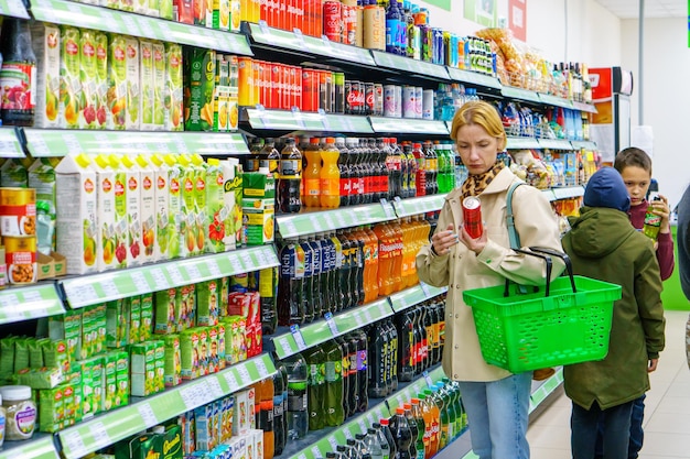 Una giovane ragazza con un cesto della spesa in mano cammina in giro per il negozio la ragazza bionda sceglie il cibo il concetto di alimentazione sana l'era del consumo