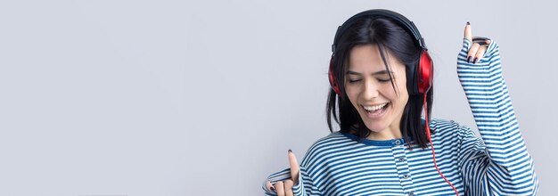 Una giovane ragazza con un giubbotto a righe sta ascoltando musica con le cuffie rosse in uno studio e ballando