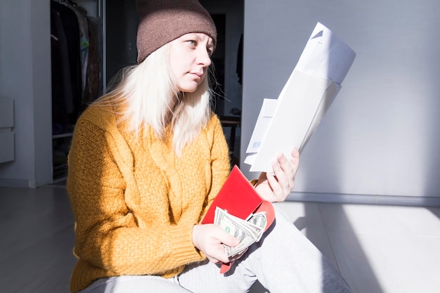 Una giovane ragazza con un maglione e un cappello gialli sta studiando grandi bollette, tasse e bollette