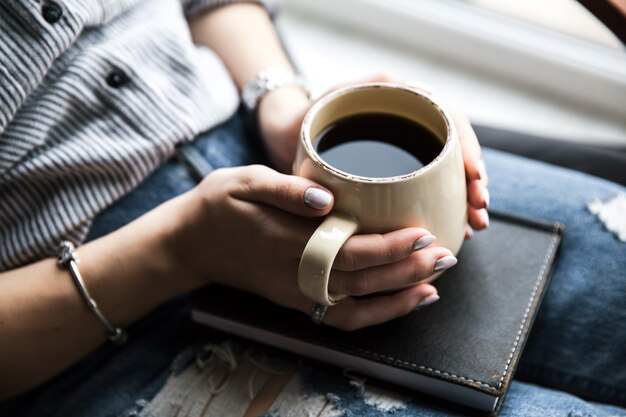 Una giovane ragazza con una bella manicure tiene un libro con una tazza di caffè. Fashion style