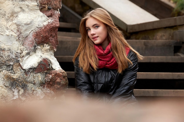 Una giovane ragazza con una gonna rossa si siede sui gradini del parco in autunno