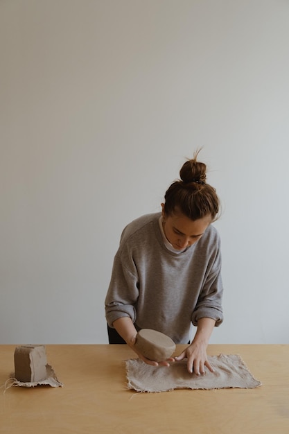 Una giovane ragazza con una manica lunga grigia realizza un vaso di argilla con le proprie mani in un laboratorio di scultura