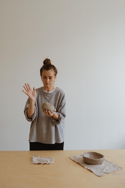 Una giovane ragazza con una manica lunga grigia realizza un vaso di argilla con le proprie mani in un laboratorio di scultura