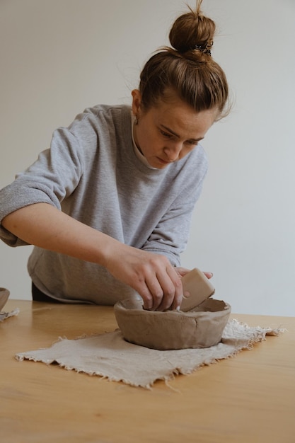 Una giovane ragazza con una manica lunga grigia realizza un vaso di argilla con le proprie mani in un laboratorio di scultura