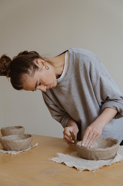 Una giovane ragazza con una manica lunga grigia realizza un vaso di argilla con le proprie mani in un laboratorio di scultura