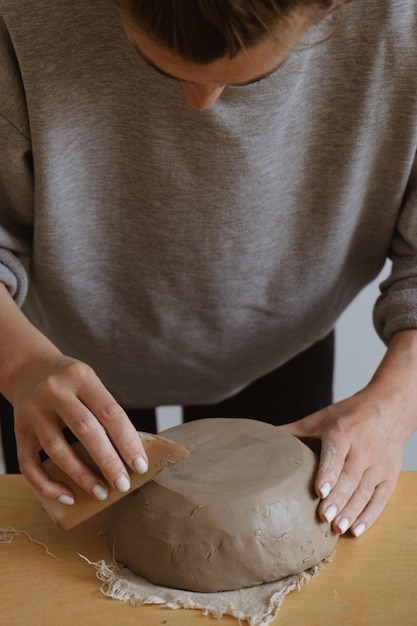 Una giovane ragazza con una manica lunga grigia realizza un vaso di argilla con le proprie mani in un laboratorio di scultura