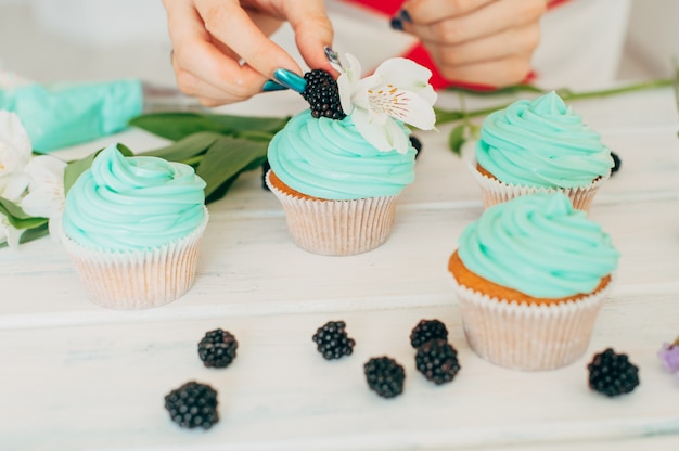 Una giovane ragazza decora cupcakes con bacche e fiori freschi