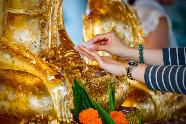 Una giovane ragazza decora una statua di Buddha in lamina d'oro in un tempio