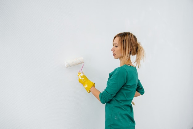 Una giovane ragazza dipinge un muro bianco con un rullo