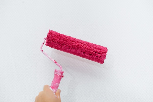 Una giovane ragazza dipinge un muro bianco in rosa con un primo piano del rullo. Riparazione degli interni.