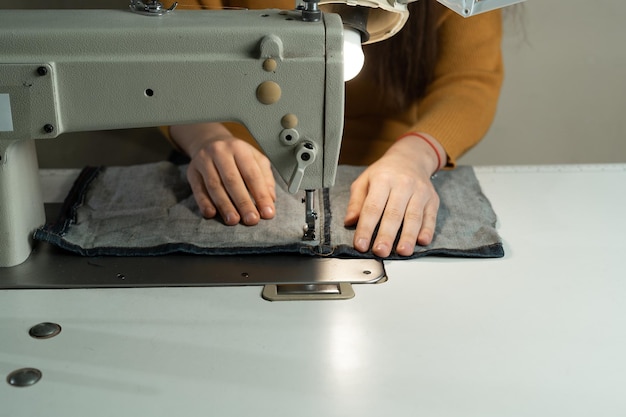 Una giovane ragazza è seduta a una macchina da cucire in officina Cucire abiti secondo il modello dell'autore Concetto di atelier di cucito Posto per il testo