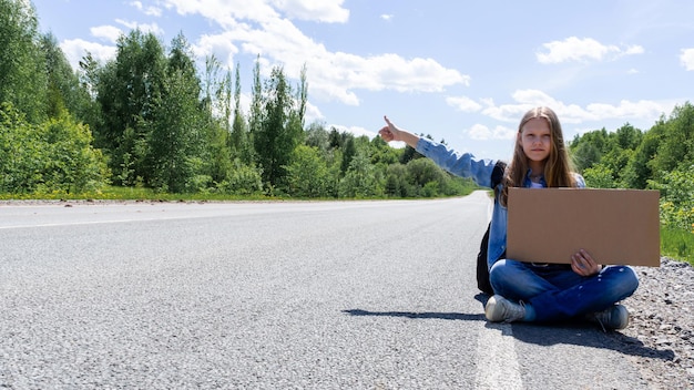 Una giovane ragazza è seduta per strada con un cartello in mano mentre fa l'autostop per il paese