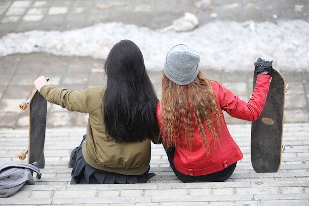 Una giovane ragazza hipster sta cavalcando uno skateboard. Amiche ragazze per una passeggiata in città con uno skateboard. Sport primaverili in strada con lo skateboard.