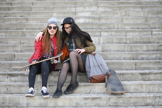 Una giovane ragazza hipster sta cavalcando uno skateboard. Amiche ragazze per una passeggiata in città con uno skateboard. Sport primaverili in strada con lo skateboard.