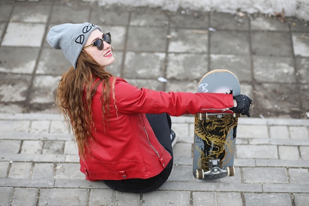 Una giovane ragazza hipster sta cavalcando uno skateboard. Amiche ragazze per una passeggiata in città con uno skateboard. Sport primaverili in strada con lo skateboard.