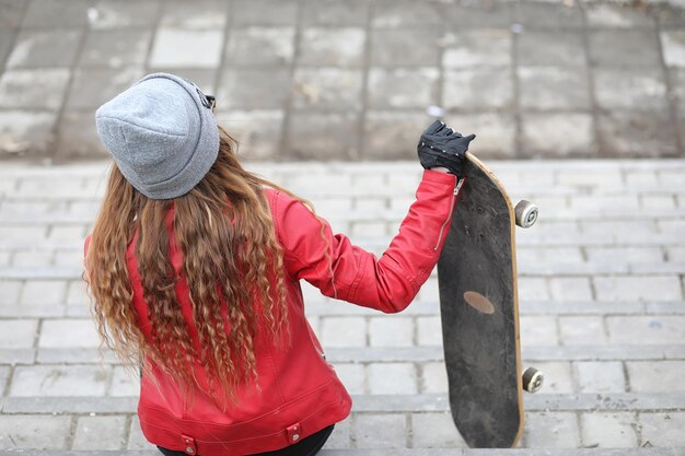 Una giovane ragazza hipster sta cavalcando uno skateboard Ragazze amiche per una passeggiata in città con uno skateboard Sport primaverili per strada con uno skateboardxA