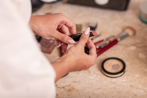 Una giovane ragazza in un accappatoio bianco in posa mentre si chiude il rossetto su uno sfondo di cosmetici sparsi.