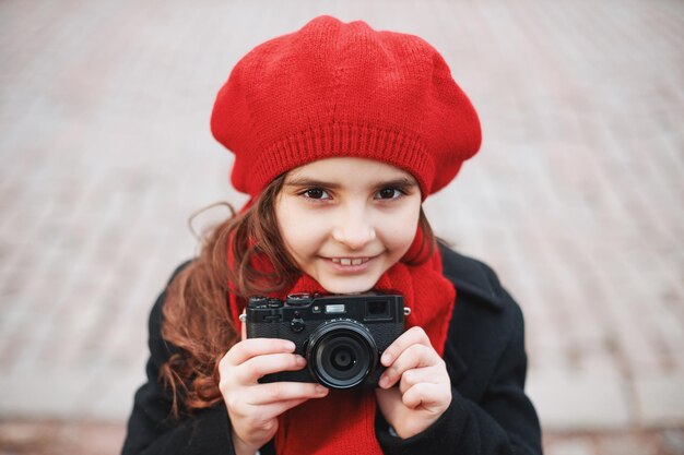 Una giovane ragazza in un berretto rosso e una sciarpa con una macchina fotografica su una strada cittadina. Foto di alta qualità