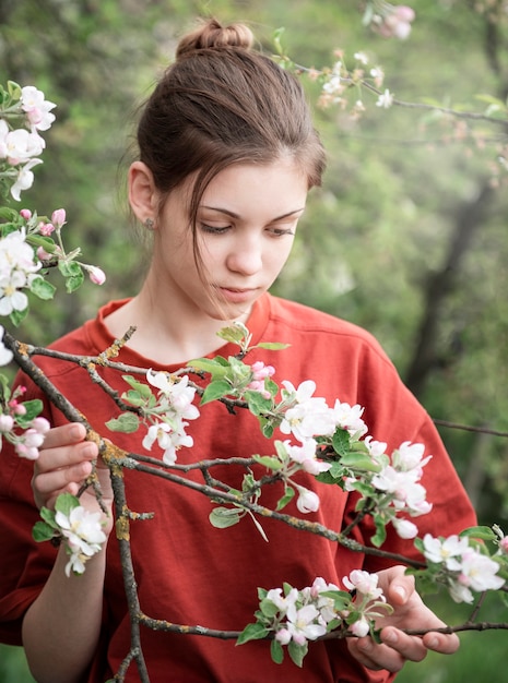 Una giovane ragazza in un giardino in fiore guarda gli alberi in fiore