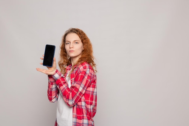 Una giovane ragazza in una camicia a quadri con un telefono su uno sfondo chiaro