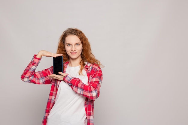 Una giovane ragazza in una camicia a quadri con un telefono su uno sfondo chiaro