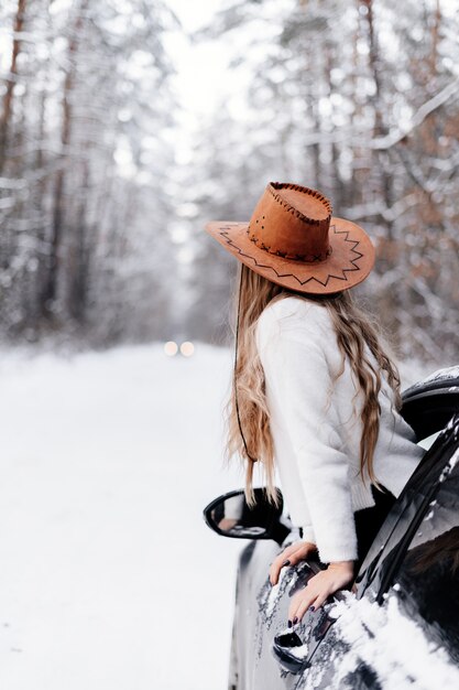 Una giovane ragazza in una foresta invernale tra la strada in macchina guarda in lontananza