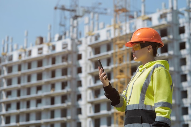 Una giovane ragazza ingegnere sta lavorando al telefono sullo sfondo della costruzione