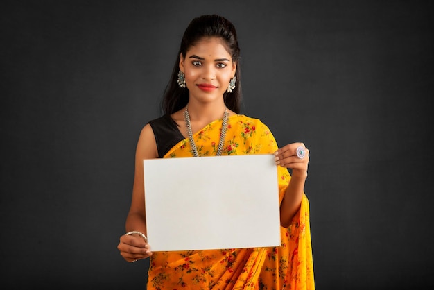 Una giovane ragazza o donna d'affari che indossa un sari e tiene in mano un cartello su uno sfondo grigio