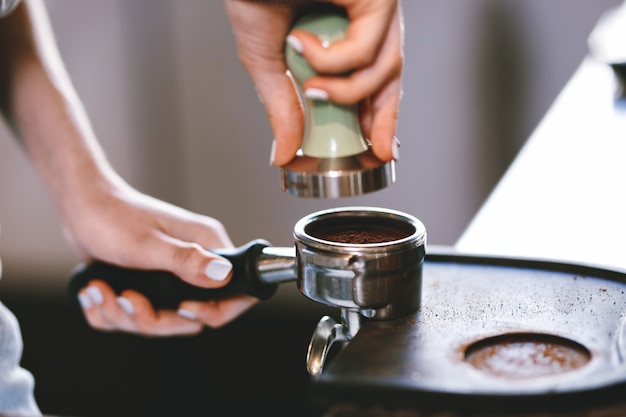 Una giovane ragazza piuttosto snella, che indossa abiti casual, sta cucinando il caffè in una moderna caffetteria. Si concentra sul processo. .