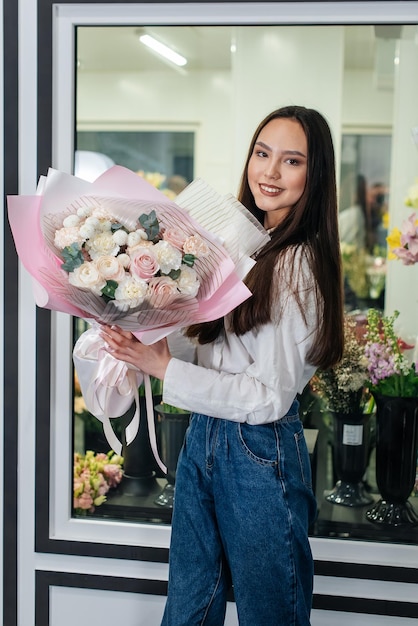 Una giovane ragazza posa con un bellissimo bouquet festivo sullo sfondo di un accogliente negozio di fiori Fiorai e bouquet in un negozio di fiori Piccole imprese