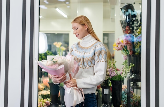 Una giovane ragazza posa con un bellissimo bouquet festivo sullo sfondo di un accogliente negozio di fiori Fiorai e bouquet in un negozio di fiori Piccole imprese