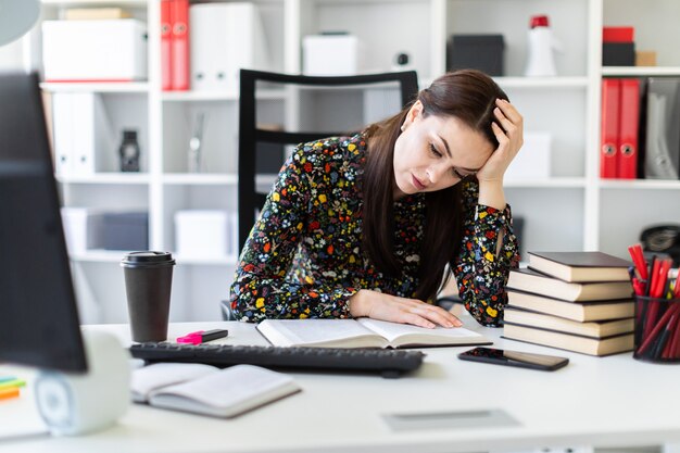 Una giovane ragazza seduta in ufficio alla scrivania del computer e lavorare con un libro.