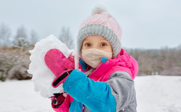 Una giovane ragazza si diverte a giocare a palle di neve in inverno di umore positivo e maschera facciale