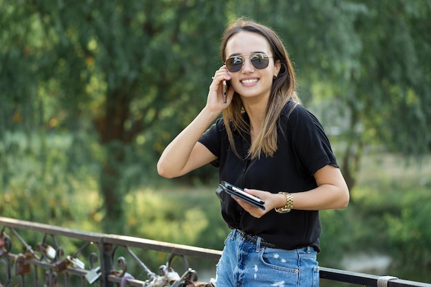 Una giovane ragazza si siede su una panchina in un parco e prende appunti Vestito in uno stile libero Donna d'affari che parla al telefono con i clienti