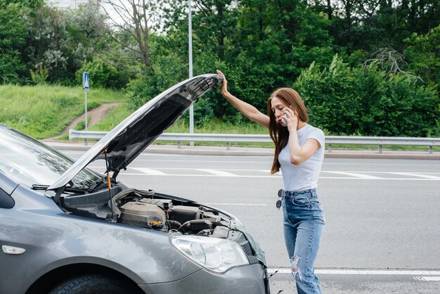 Una giovane ragazza si trova vicino a un'auto in panne in mezzo all'autostrada e chiede aiuto al telefono. Guasto e guasto dell'auto. In attesa di aiuto.