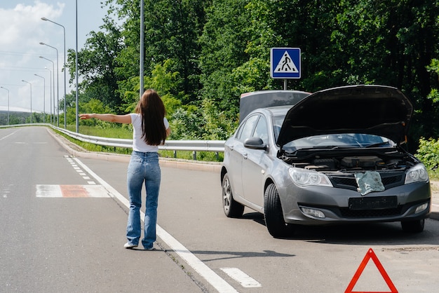 Una giovane ragazza si trova vicino a un'auto rotta nel mezzo dell'autostrada e chiede aiuto al telefono, mentre cerca di fermare le auto che passano. Guasto e guasto dell'auto. In attesa di aiuto.