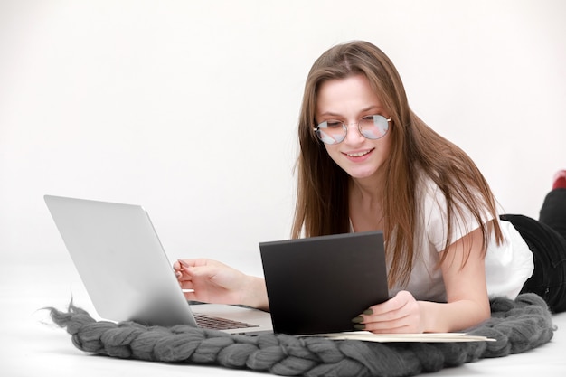 Una giovane ragazza sorridente con gli occhiali si siede con un computer portatile. Istruzione, lavoro a distanza e blog. Isolato su uno sfondo bianco.