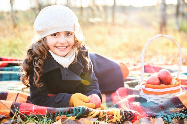 Una giovane ragazza sorridente con un cappotto blu giace su una coperta nel parco in autunno. Foto di alta qualità