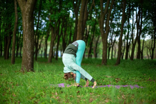 Una giovane ragazza sportiva pratica yoga in una foresta estiva verde chiusa, yoga assans postura. Meditazione e unità con la natura