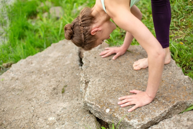 Una giovane ragazza sportiva pratica yoga in una posizione tranquilla sulla riva del fiume in estate, in una posa di asana yoga. Meditazione e unità con la natura