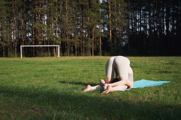 Una giovane ragazza sta facendo yoga nella foresta all'aperto in una soleggiata giornata estiva Una ragazza sta in un rack esegue un'asana nel parco Concetto di meditazione di stile di vita sano Bellezza e salute delle donne