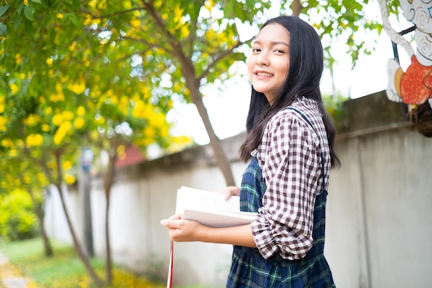 Una giovane ragazza tiene un libro e sta sotto un bellissimo albero