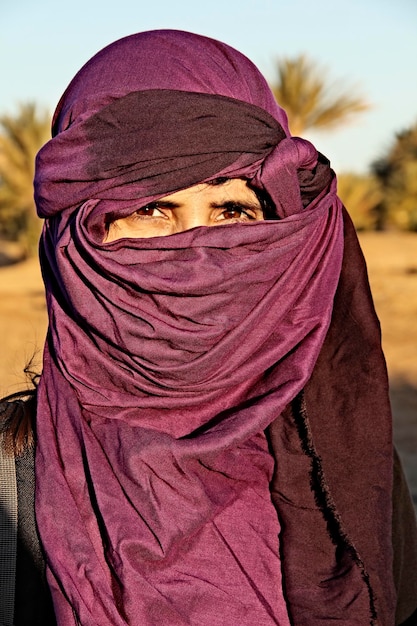 Una giovane ragazza turistica europea con sciarpa berbera viola nel deserto di Merzouga