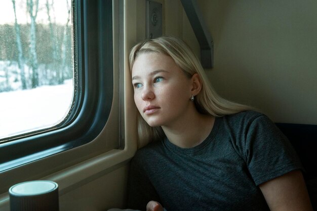 Una giovane ragazza viaggia in un compartimento del treno e guarda fuori dalla finestra Triste bella ragazza bionda in una maglietta grigia Closeup Viaggi e istruzione