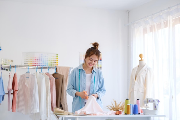 Una giovane stilista asiatica sta tagliando il tessuto e prepara un modello per una nuova collezione