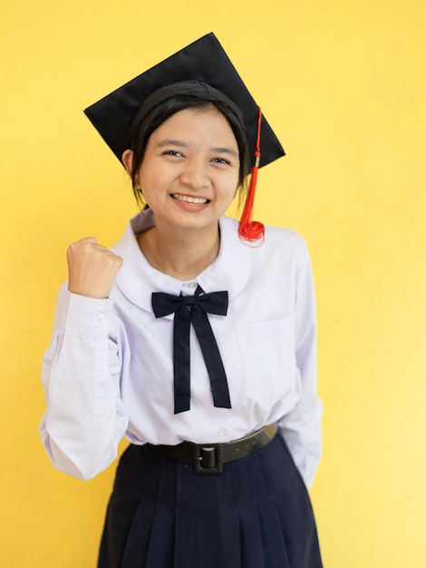 Una giovane studentessa felice indossa un cappello di laurea su sfondo giallo