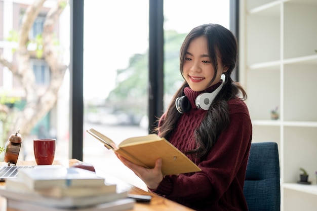 Una giovane studentessa universitaria asiatica felice sta leggendo un libro a un tavolo nella caffetteria