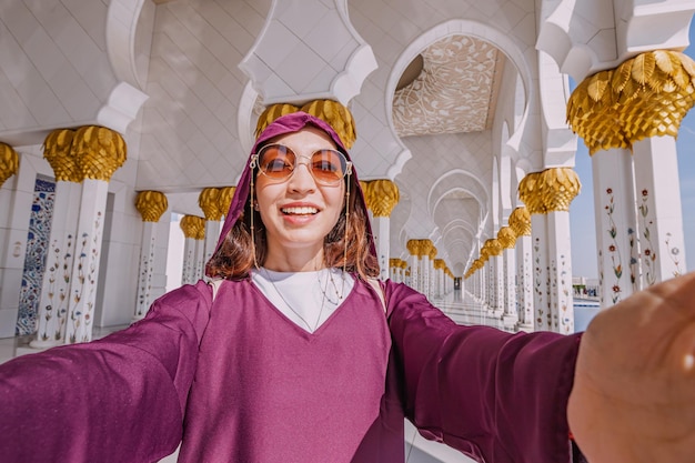 Una giovane turista che indossa un Abaya tradizionale cattura il suo viaggio attraverso la Grande Moschea di Sheikh Zayed con un selfie